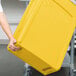 A person holding a yellow Rubbermaid Slim Jim rectangular trash can with a lid.