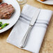 A Walco stainless steel dinner knife on a white napkin next to a plate of food.