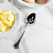A bowl of butter with a Walco Sentry Pierced Serving Spoon on a marble surface.
