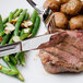A Walco stainless steel table knife on a plate of steak, potatoes, and green beans.