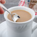 A person holding a Walco stainless steel demitasse spoon in a white mug of coffee.