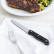 A Libbey steak knife and fork next to a plate of steak and vegetables.