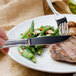 A fork cutting into a steak on a plate with a Walco Prim steak knife.