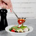 A hand using a Walco stainless steel gravy ladle to pour sauce over a bowl of salad.