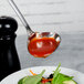 A Walco stainless steel gravy ladle spooning red sauce over a plate of salad.