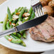 A plate of food with meat, green beans, and potatoes with a Walco stainless steel dinner knife.