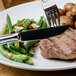 A Walco Ultra stainless steel steak knife on a plate of food with meat, potatoes, and green beans.