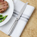 A Walco stainless steel table knife on a napkin next to a plate of steak and green beans.
