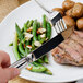 A Walco Maremma stainless steel table knife next to a plate of food with a steak and green beans.