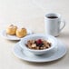 A Tuxton Alaska bright white china plate with cereal, a pastry, and a cup of coffee on a table.