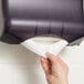 A hand pulling a white premium C-fold towel from a dispenser.