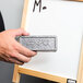 A hand using a silver rectangular Expo dry erase eraser on a white board.