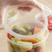 A hand holding a Choice translucent plastic deli container of fruit.
