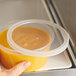 A hand holding a Choice translucent plastic deli lid over a container of food.