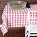 A table with a bowl of salad and a red and white checkered vinyl tablecloth on a table outdoors.