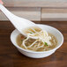 A hand holding a Thunder Group Blue Bamboo soup ladle over a bowl of noodle soup.