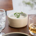 A Chef & Sommelier white stackable bowl filled with soup and topped with green leaves on a table.