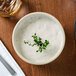 A white stackable bowl of soup with a sprig of thyme.
