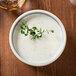 A white Chef & Sommelier stoneware bowl filled with soup and a sprig of herb.