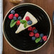 A Chef & Sommelier Geode black stoneware plate with a slice of cheesecake and berries.