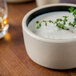 A white Chef & Sommelier stoneware bowl filled with soup and topped with a sprig of green plant.