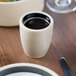 A Chef & Sommelier black stoneware espresso cup filled with liquid on a table.