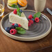 A slice of cheesecake with berries on a Chef & Sommelier grey stoneware plate.