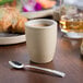 A Chef & Sommelier white stoneware espresso cup filled with coffee on a table with a spoon.