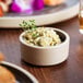 A Chef & Sommelier stackable stoneware ramekin filled with food on a table with a sprig of herb.