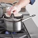 A person wearing gloves uses a Vigor stainless steel sauce pan on a stove.