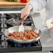 A person cooking meatballs in a Vigor stainless steel fry pan.