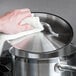 A hand using a white towel to put a stainless steel lid on a pot.