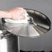 A hand using a towel to clean a stainless steel pot lid.