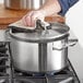A person holding a Vigor stainless steel sauce pot with a rag over the lid on a stove.