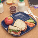 A Carlisle blue 4 compartment tray with a sandwich, apple, and vegetables.