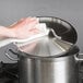 A person using a towel to wipe a Vigor stainless steel stock pot lid.