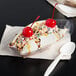 A banana split in a clear plastic boat with cherries and sprinkles on top.