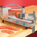 A Nemco tomato slicer machine with a tomato on a cutting board.