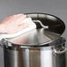 A hand using a white towel to clean a stainless steel Vigor lid
