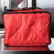 A Rubbermaid ProServe red insulated delivery bag with a black strap sits on a counter.