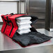 A red and black Rubbermaid insulated delivery bag with white food containers inside.