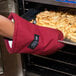A hand using a San Jamar Cool Touch Flame oven mitt to hold a metal tray of french fries.