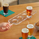 A hand holding an Acopa Acrylic Drop-In Flight Paddle with beer glasses on a table.