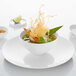 A bowl of soup with noodles and green leaves on a white Villeroy & Boch bone porcelain plate.