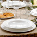 A table set with Villeroy & Boch white bone porcelain deep plates, glasses, and silverware.