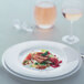 A Villeroy & Boch white bone porcelain flat plate with food and wine on a table.