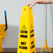 A person holding a yellow Rubbermaid caution wet floor cone sign.