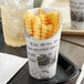 A Choice paper scoop cup with a newsprint design filled with french fries.