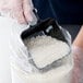 A person in gloves using a Carlisle black polycarbonate portion scoop to fill a plastic container with rice.