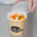 A hand placing a vented plastic lid on a container of orange and green food.